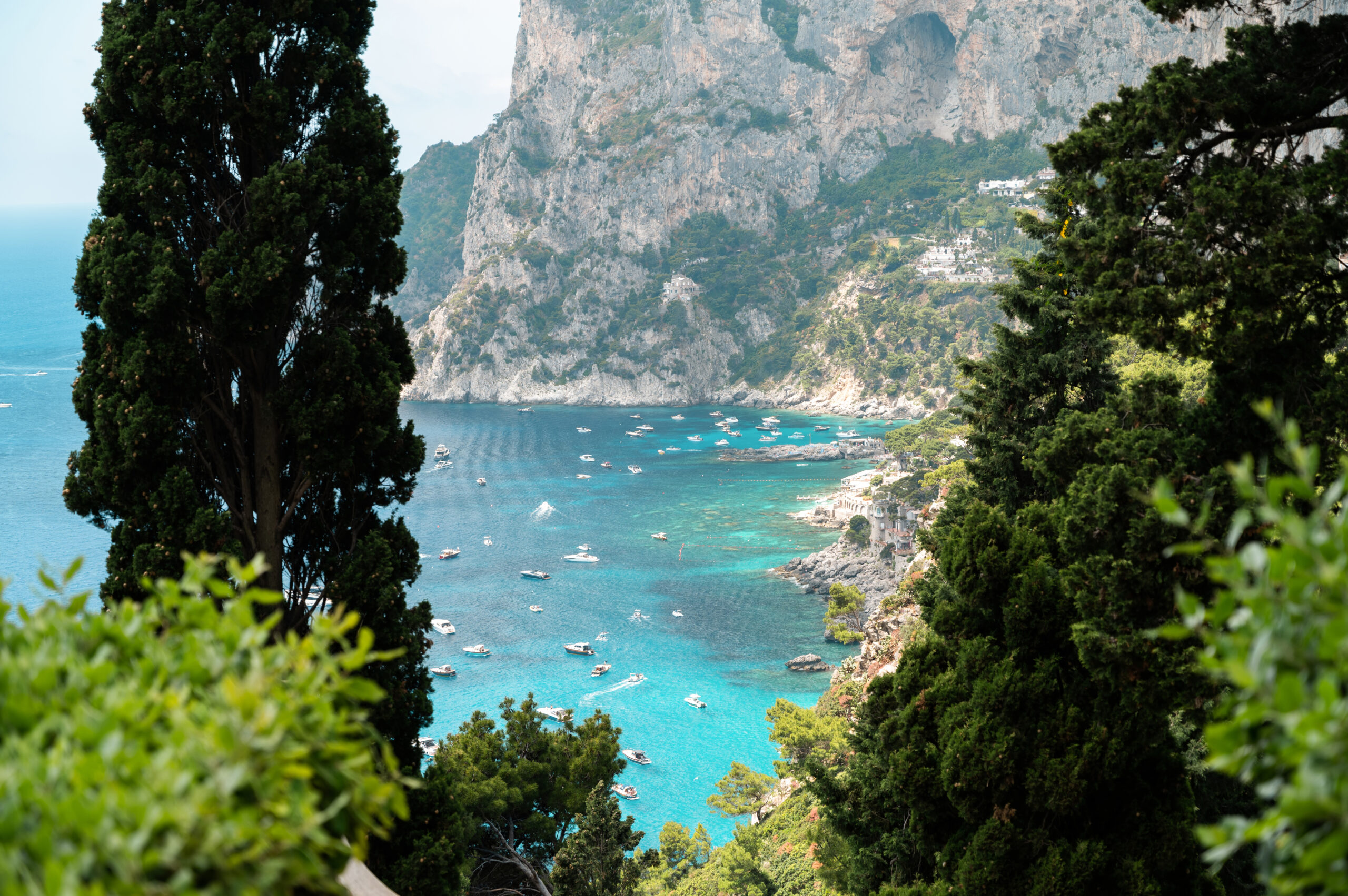 Tyrrhenian sea coast of Capri, Italy. Rocky cliffs, blue water, multiple floating boats, greenery