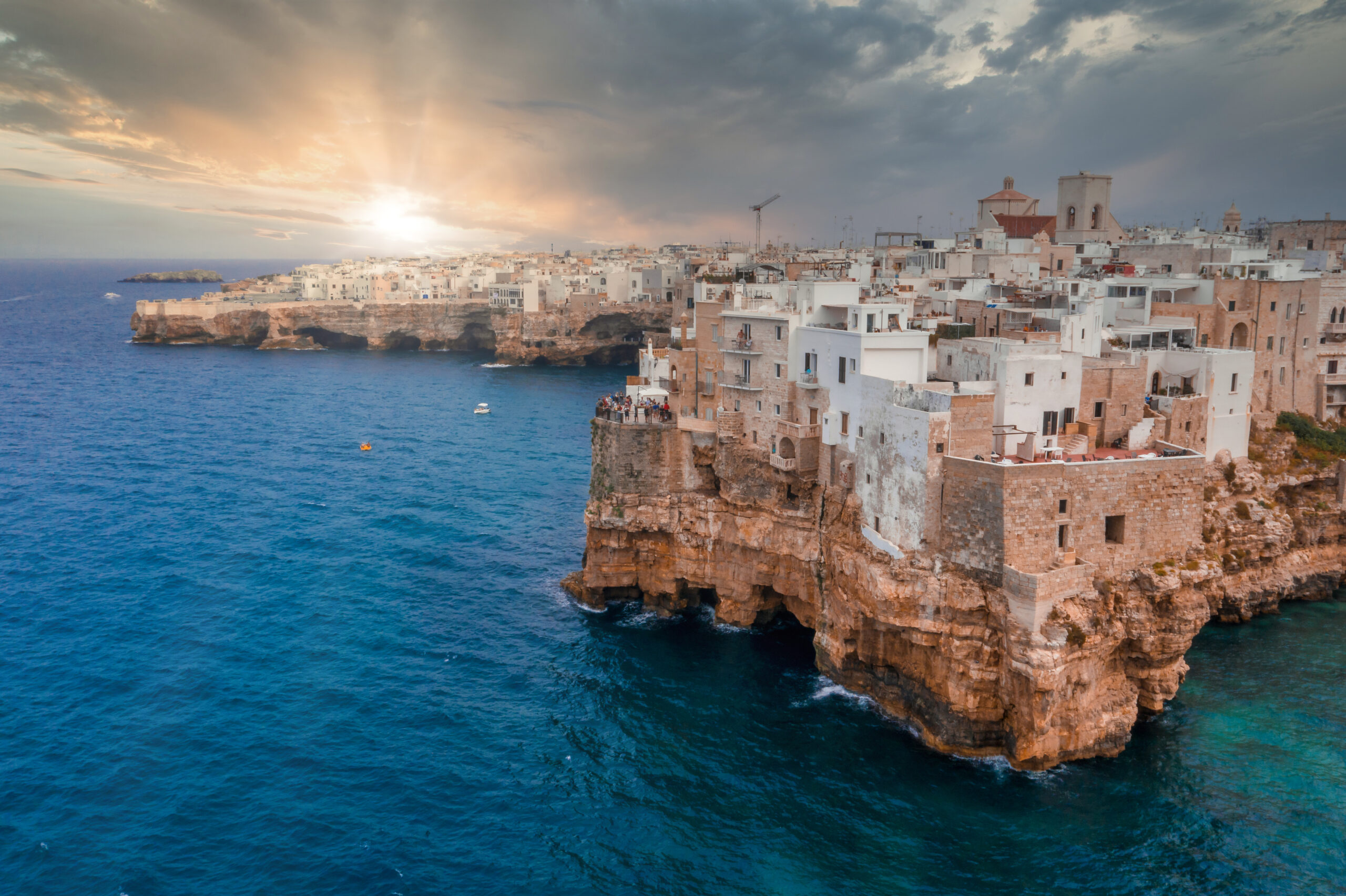 A cityscape of Polignano a Mare surrounded by the sea under the sunlight and a cloudy sky in Italy